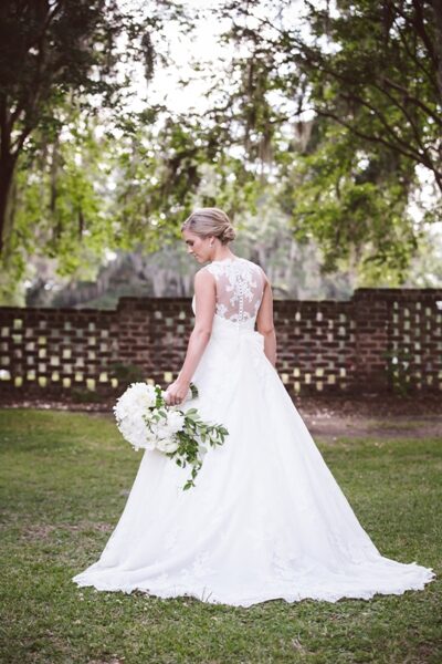 Bride in elegant white dress holding bouquet outdoors.