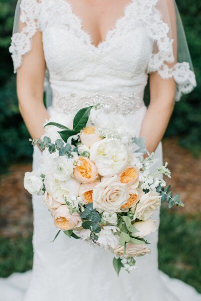 Bride holding a bouquet of white and peach roses with greenery.