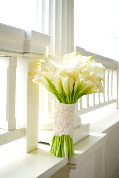 A bouquet of white calla lilies wrapped in lace on a balcony railing.