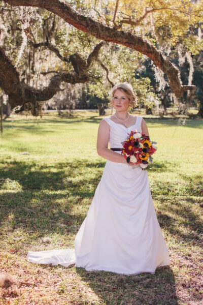 Bride in white dress holding colorful bouquet outdoors.
