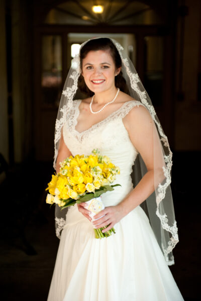 Smiling bride in white dress holding yellow bouquet.