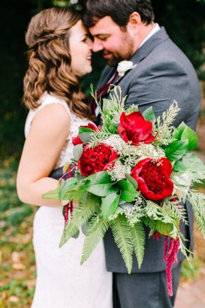 Bride and groom embracing with a vibrant bouquet of red and white flowers.