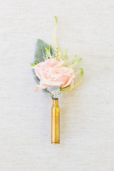 A delicate boutonniere with a pale pink rose and greenery in a gold holder.