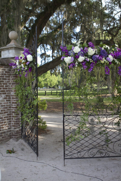 Decorated wrought iron gate with purple and white flowers for an event.