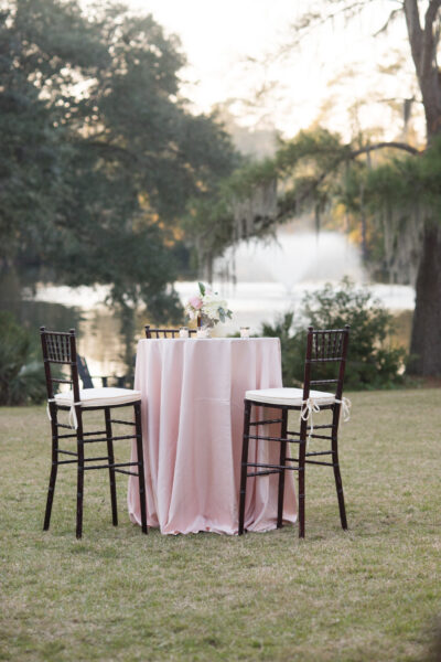 Elegant outdoor table setup with two chairs and a pink tablecloth near a fountain.