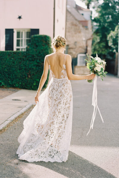 Bride in a lace wedding dress holding a bouquet walking outside.