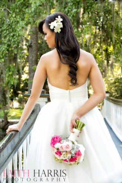Bride in a strapless white gown holding a bouquet on a wooden bridge.