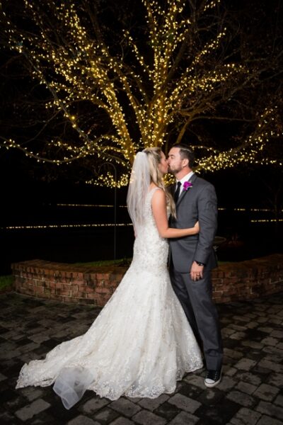 Bride and groom embrace under fairy lights at night.