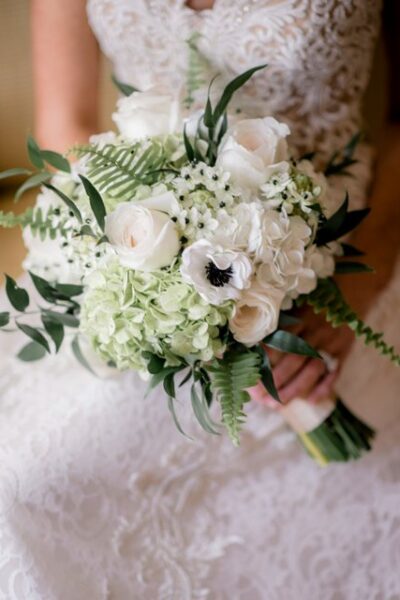 Close-up of a bride holding a white floral bouquet with greenery.