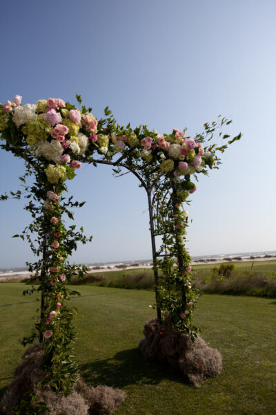 A floral archway with pink flowers set in a grassy field under a clear sky.