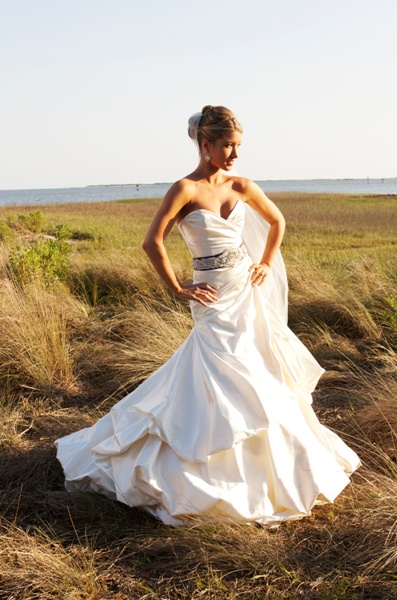 Bride in a strapless white wedding gown standing outdoors in a field.