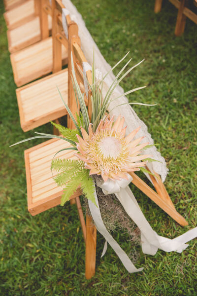 Elegant wooden chair decorated with white flower and green leaves for outdoor event.