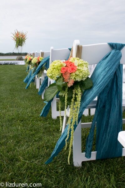 Elegant white chairs decorated with blue ribbons and colorful flowers for an outdoor event.