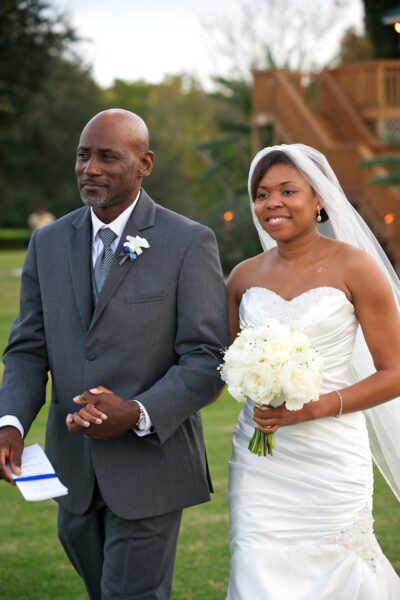 Bride and groom smiling, holding hands outdoors on their wedding day.