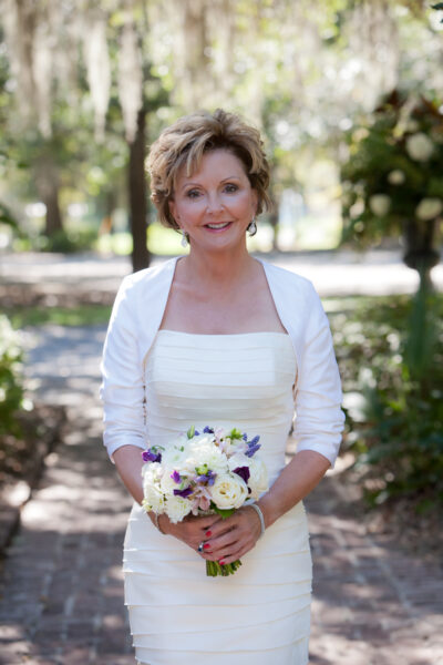 Smiling bride in white dress holding a bouquet outdoors.