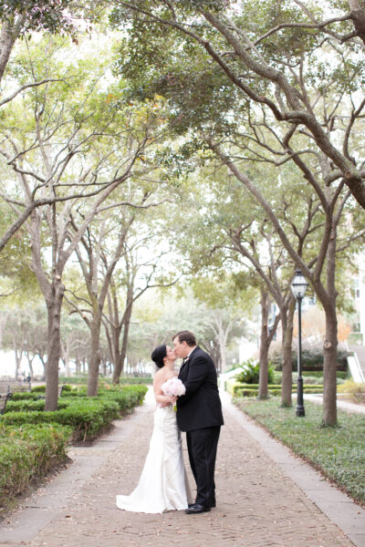 A couple shares a romantic kiss under a canopy of trees.