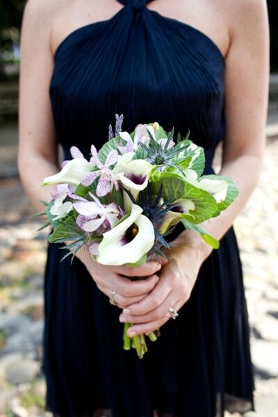 Person in black dress holding a bouquet of white and purple flowers.