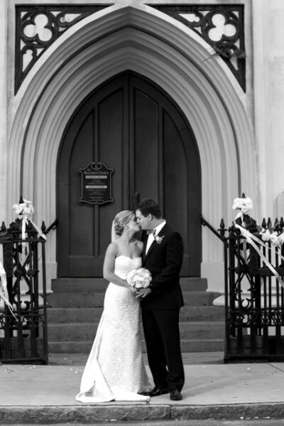 Black and white photo of a bride and groom kissing on church steps.