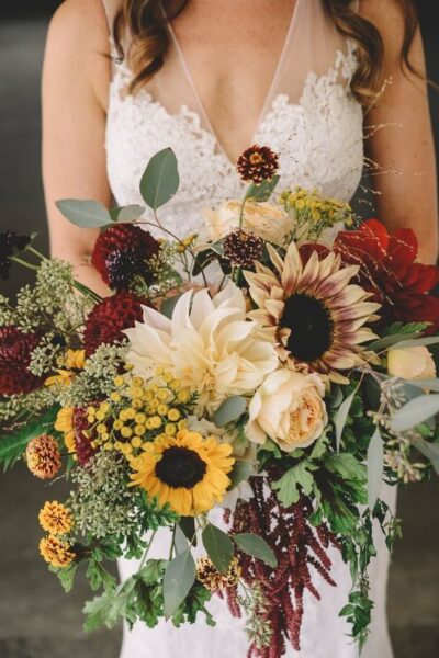 Bride holding a vibrant bouquet with sunflowers and assorted flowers.