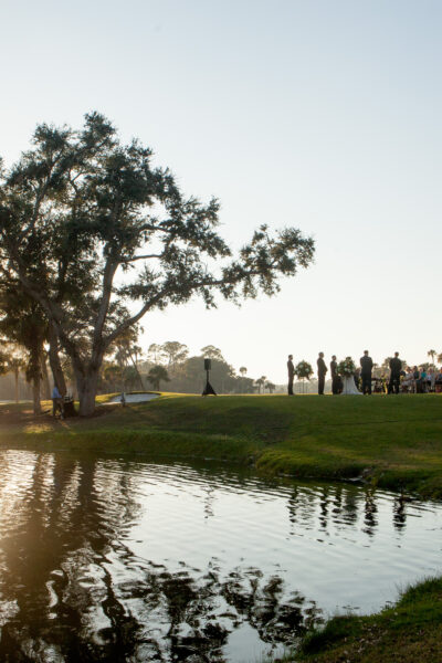 People gathered near a pond at sunset with trees and reflections.