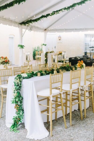 Elegant wedding reception setup with gold chairs and lush greenery.