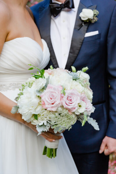 Bride holding a bouquet of white and pink flowers next to groom in a suit.