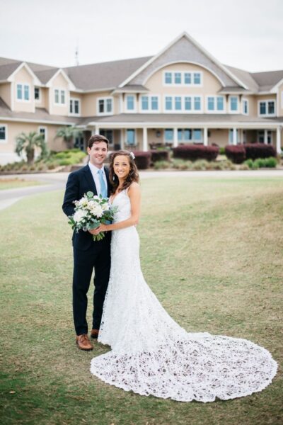 Bride and groom posing outdoors in front of a large house.