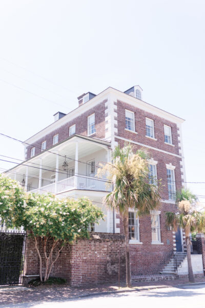 Sunlit three-story brick building with wraparound balconies and palm trees.