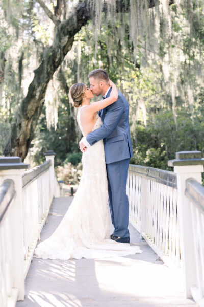 Bride and groom share a kiss on a sunlit bridge during their wedding.