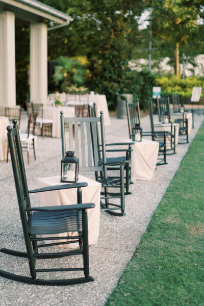 Row of black rocking chairs with lanterns along a garden path.