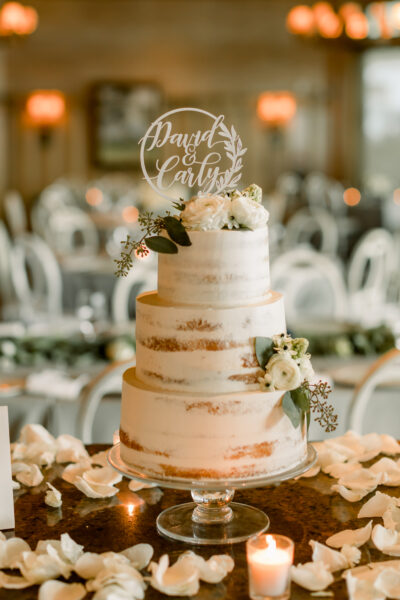 Elegant semi-naked wedding cake adorned with flowers and a custom topper.