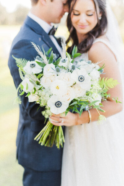Bride holding a white and green floral bouquet on wedding day.