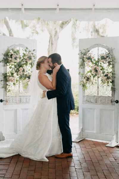 Bride and groom share a romantic kiss in front of floral doors.