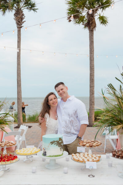 Smiling couple standing together near a decorated table at a beachside event.