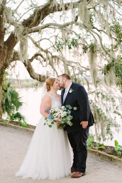A bride and groom share a kiss outdoors on their wedding day.