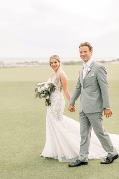 Bride and groom holding hands outdoors, smiling joyfully.