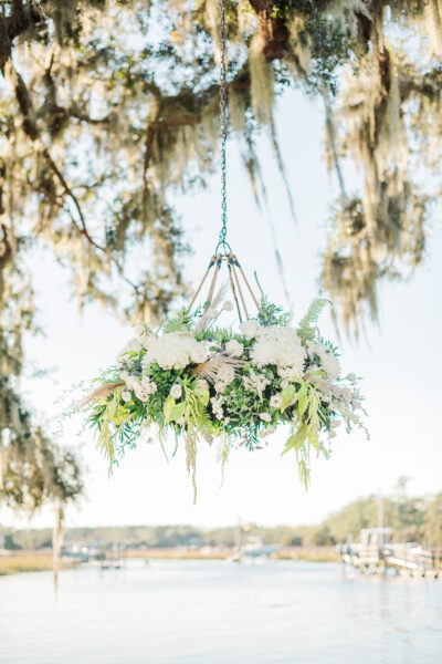 Elegant floral chandelier hanging outdoors with white and green flowers.