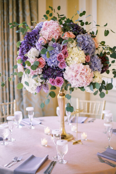 Elegant floral centerpiece with pastel blooms on a gold stand at a formal event.