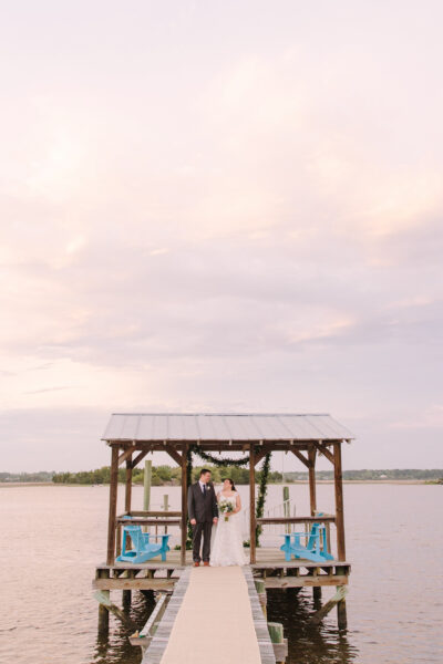 A wooden pier leading to a small hut on calm water during sunset.