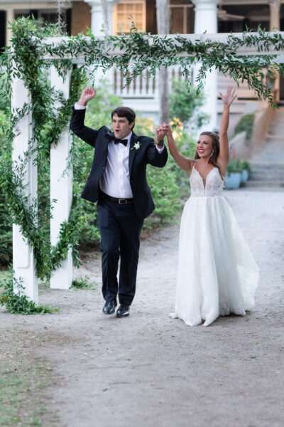Newlyweds joyfully walk hand in hand outdoors after their wedding ceremony.
