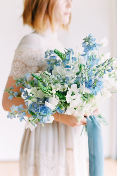 A bride holding a bouquet of white and blue flowers.