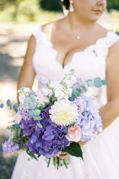 Bride holding a vibrant bouquet of purple, white, and green flowers.