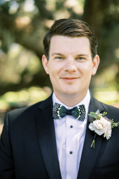 A man in a tuxedo with a floral bow tie and boutonniere.