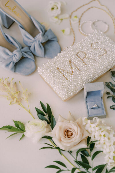 Elegant bridal accessories including shoes, a beaded clutch, and floral arrangements.