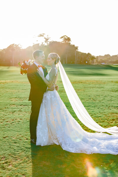 A bride and groom share a kiss on a sunny golf course.