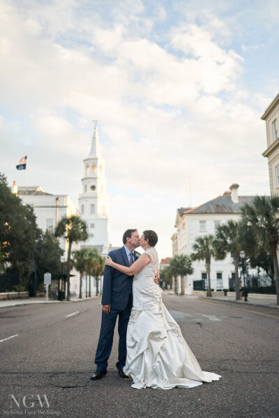 A couple embraces in a charming town square with a church steeple in the background.