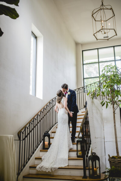 Bride and groom embrace on a stairway in a bright, elegant venue.