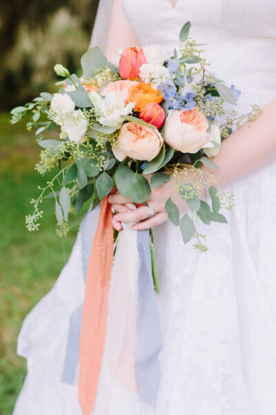 Bride holding a delicate bouquet with peach roses and greenery.