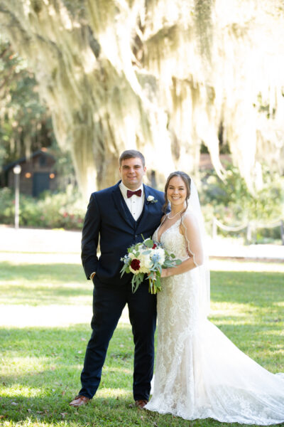 Newlywed couple posing outdoors in elegant wedding attire.