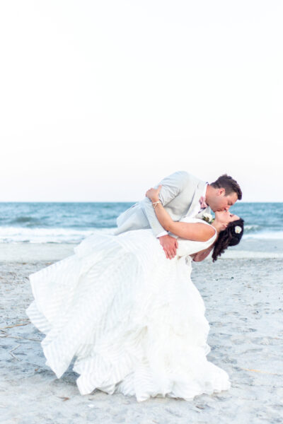 Bride and groom sharing a romantic dip kiss on the beach.
